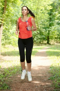 Fitness girl jogging through the woods in summer.